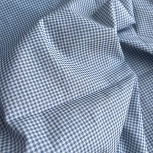 May include: Close-up of blue and white gingham fabric. The fabric is folded and draped, showing the texture and pattern of the woven material. The pattern is a classic small check design.