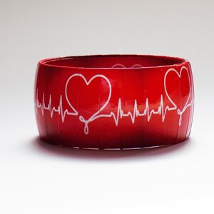 May include: Red bangle bracelet with a white heart and EKG line design.