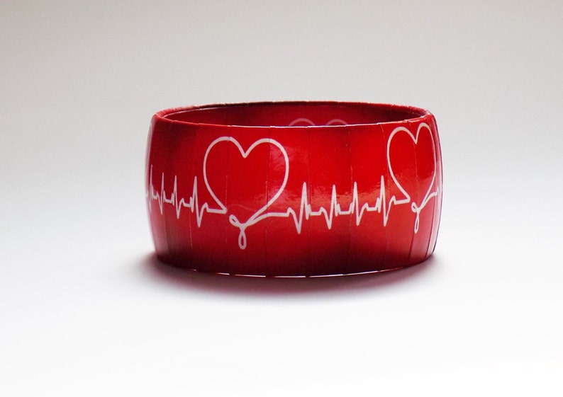 May include: Red bangle bracelet with a white heart and EKG line design.