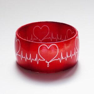 May include: Red bangle bracelet with a white heart beat design and white hearts.