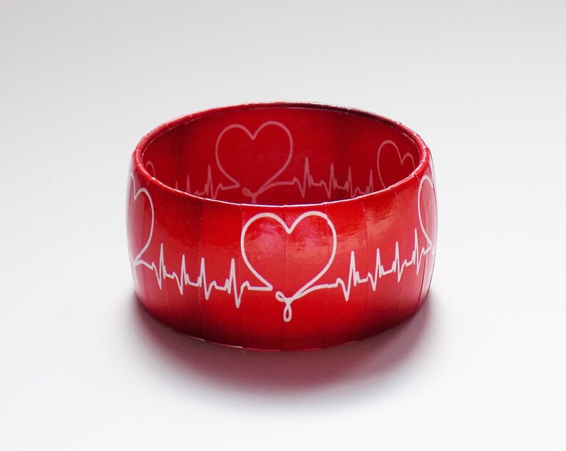 May include: Red bangle bracelet with a white heart beat design and white hearts.