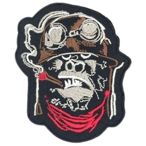 May include: Embroidered patch featuring a cartoon character wearing goggles and a bandana, smoking a cigarette. The character has a brown hat and a red bandana. The patch is on a black background.