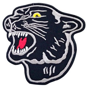 May include: Black and white embroidered iron-on patch of a snarling panther head with a yellow eye.