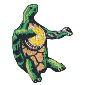May include: An embroidered patch depicting a green turtle playing a banjo. The turtle is standing with its legs outstretched and its head tilted to the side. The banjo is yellow with a brown rim and has strings.