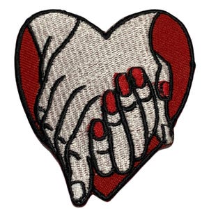 May include: Embroidered iron-on patch featuring two hands clasped together in the shape of a heart. The hands are white with black outlines and red nail polish. The heart is red.