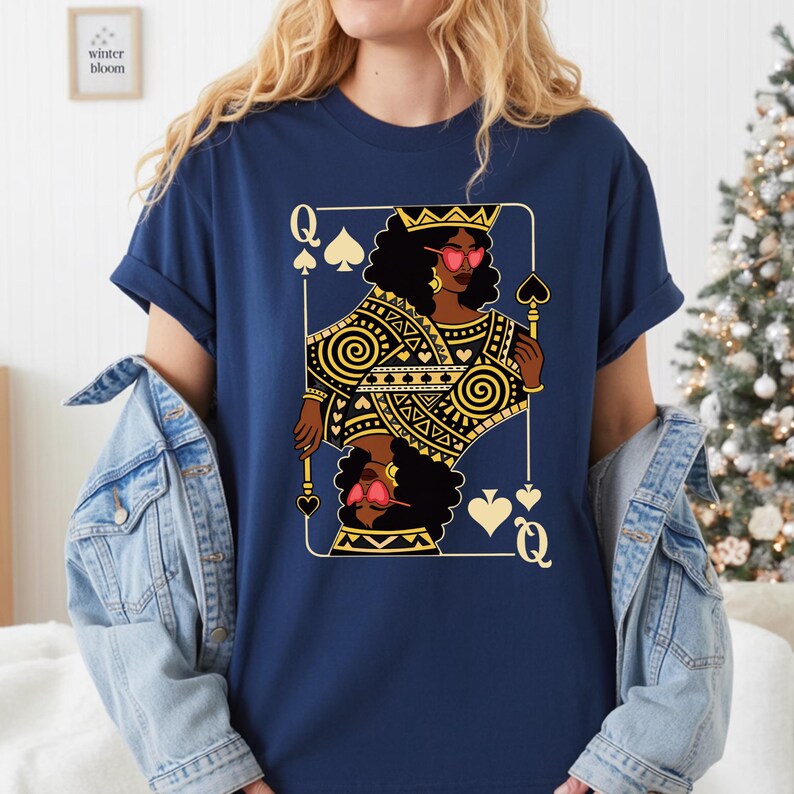 May include: Navy blue t-shirt with a Queen of Spades playing card design. The card shows a woman with a crown and heart-shaped sunglasses, holding a scepter. The design is in gold and black, with the text "winter bloom" in the upper left corner.
