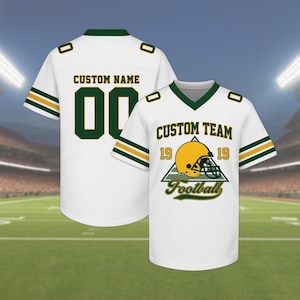 May include: White football jersey with green and gold accents. The jersey features the text "CUSTOM NAME" and the number "00" on the back. The front displays "CUSTOM TEAM" with a football helmet graphic and the word "Football".