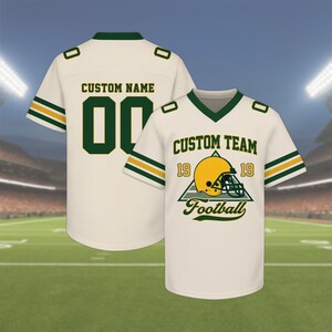 May include: Two cream-colored football jerseys. One jersey has the text "CUSTOM NAME" and the number "00" in green. The other jersey has the text "CUSTOM TEAM" and a football helmet graphic. Both jerseys have green and yellow stripes.