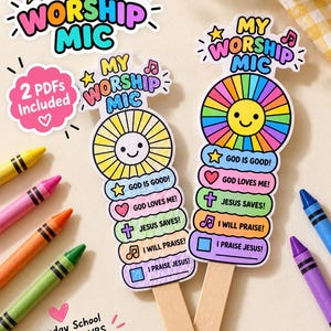 May include: Two paper microphone-shaped crafts on wooden sticks, featuring a sun graphic and text including "MY WORSHIP MIC," "GOD IS GOOD!," "GOD LOVES ME!," "JESUS SAVES!," "I WILL PRAISE!," and "I PRAISE JESUS!" with colorful crayons nearby.