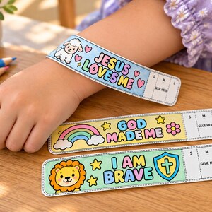 May include: Three paper wristbands featuring colourful cartoon illustrations and text. One blue band says Jesus Loves Me with a lamb, one yellow band says God Made Me with a rainbow, and one green band says I Am Brave with a lion and a cross shield.