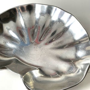 May include: A silver metal serving dish shaped like a seashell. The dish has a smooth, reflective surface and a scalloped edge.