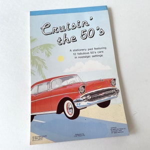 May include: A red and white 1950s car with chrome accents is driving on a road with palm trees and a blue sky. The car is featured on a stationery pad with the text "Cruisin' the 50's" and "A stationery pad featuring 12 fabulous 50's cars in nostalgic settings".