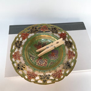 May include: A decorative brass bowl with a green, gold, black, and red floral design. The bowl has a cut-out pattern around the edge.