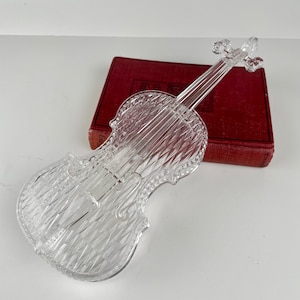 May include: A clear glass violin shaped dish. The dish has a diamond pattern and is sitting on top of a red book.