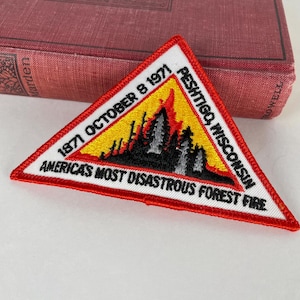 May include: A triangular patch with a red border and white background. The patch features text that reads "1871 October 8 1971 Peshtigo, Wisconsin America's Most Disastrous Forest Fire". The center of the patch depicts a forest fire with yellow and red flames.