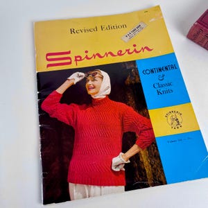 May include: A vintage knitting pattern book titled "Spinnerin" with a woman wearing a red sweater on the cover. The book has a yellow and blue design with the text "Continental & Classic Knits."