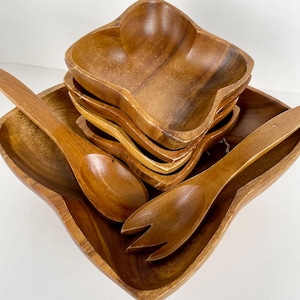 May include: A wooden salad serving set featuring a large square bowl, six smaller flower-shaped bowls, and wooden serving spoons and a fork. The set is made of a warm, medium-toned wood.