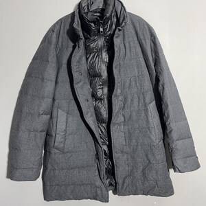 May include: A gray quilted jacket with a black inner lining and a zipper closure. The jacket has a stand-up collar and a long sleeve design.