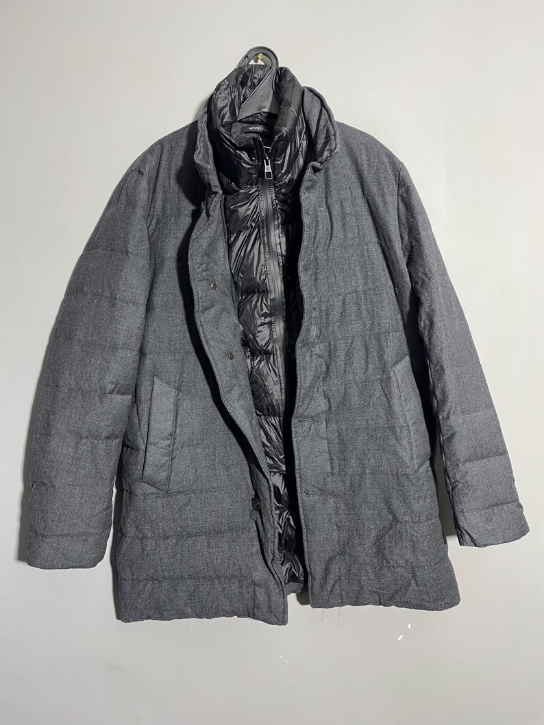 May include: A gray quilted jacket with a black inner lining and a zipper closure. The jacket has a stand-up collar and a long sleeve design.
