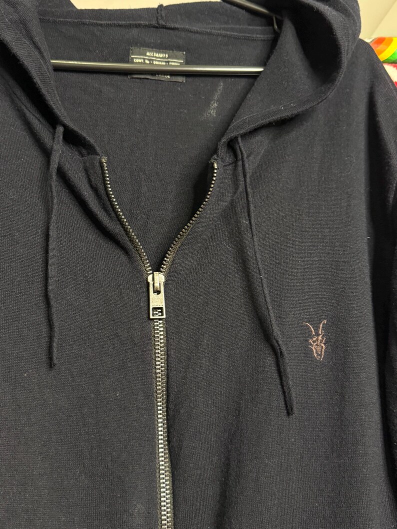 May include: A navy blue zip-up hoodie with a drawstring hood and a small embroidered logo on the chest. The hoodie has a full-length zipper and is hanging on a hanger.