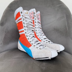 May include: Pair of high-top sneakers with a white, orange, and blue color scheme. The sneakers feature a lace-up design, the Puma logo, and a unique design with a mix of materials.