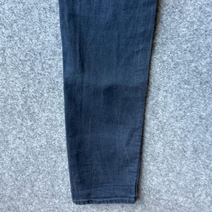 Op de afbeelding: Een enkele broekspijp gemaakt van donker antracietgrijze denimstof. Het materiaal heeft een zichtbare keperbinding en een recht model dat iets taps toeloopt naar de onderzoom. De stof vertoont een subtiele vervaging en een consistente donkere tint.