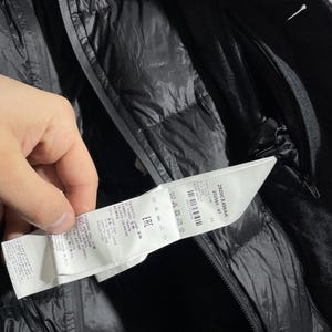 May include: A black puffer jacket with a black wool outer layer. The jacket has a zipper closure and a label with the text "2920CX498AK 202580-97 54 WARZ M EAC".