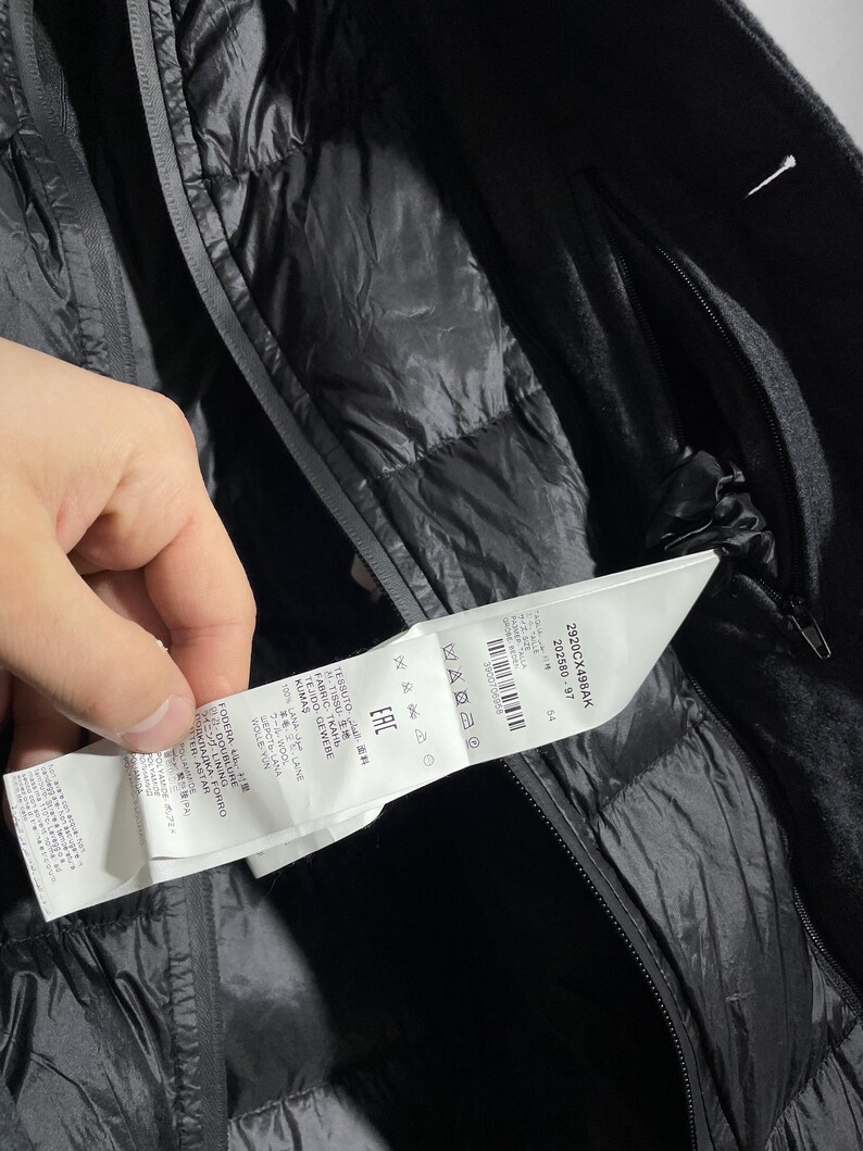 May include: A black puffer jacket with a black wool outer layer. The jacket has a zipper closure and a label with the text "2920CX498AK 202580-97 54 WARZ M EAC".