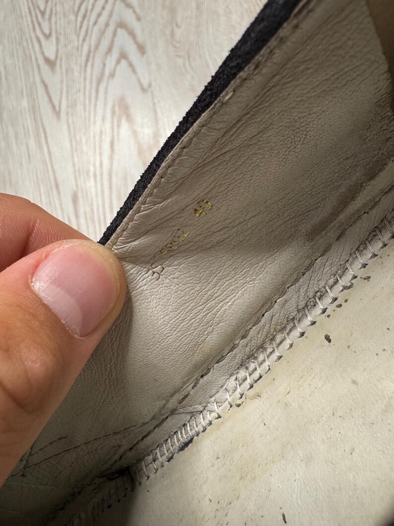 May include: Close-up of the inside of a black shoe. The interior is light beige leather with a stitched seam along the edge. The number "45" is stamped in gold near the heel.