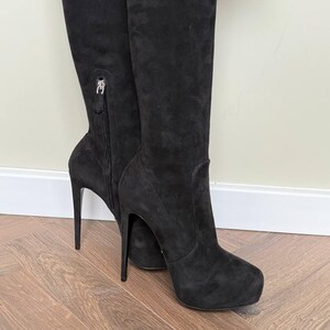 May include: Black suede over-the-knee boots with stiletto heels. The boots have a zipper detail on the side and a platform sole. The heels are approximately 5 inches (12.7 cm) high.