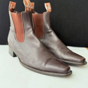 May include: A pair of brown leather ankle boots with elastic side panels and a small heel. The boots have a pull tab at the top with the brand name. The boots are made of a smooth, dark brown leather.