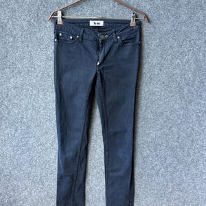 Op de afbeelding: Donkergrijze denim jeans met een klassiek five-pocket ontwerp, een knoop- en ritssluiting en een wit binnenlabel met de merknaam Acne in het zwart gedrukt, opgehangen aan een metalen kledinghanger met twee clips.