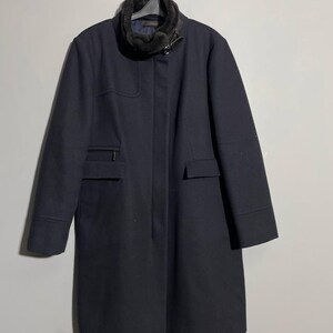 May include: A long, dark blue coat with a faux fur collar and a buckle closure. The coat has two pockets on the front and a zippered pocket on the left side.