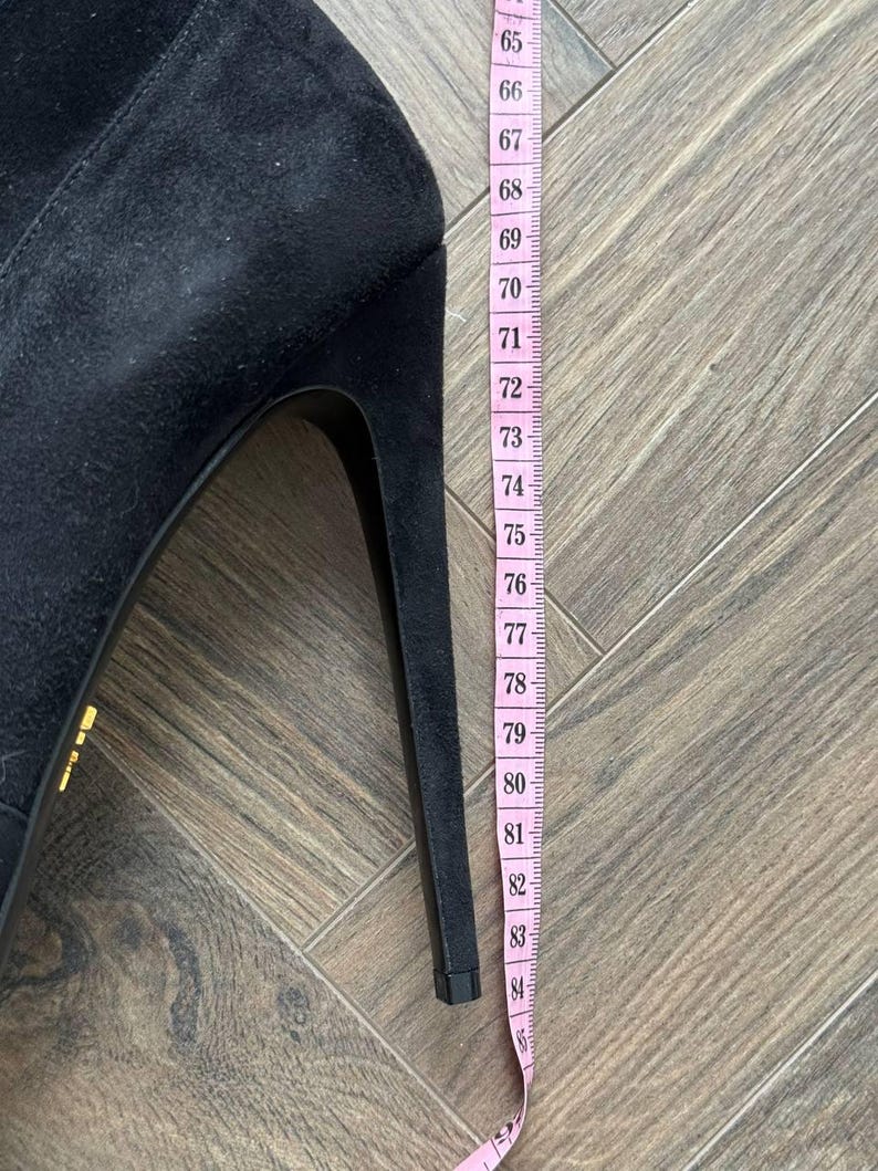 May include: A black suede high-heeled shoe with a stiletto heel. A pink measuring tape shows the heel height is approximately 3.3 inches. The shoe has a pointed toe and a sleek, elegant design.