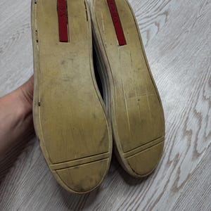 May include: A pair of worn sneakers with off-white soles and a red accent on the heel. The soles are dirty, showing signs of wear and use. The shoes are likely casual footwear.