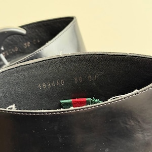 Op de afbeelding: Close-up van de binnenkant van een zwarte leren schoen. De schoen heeft een zwarte binnenzool met de nummers "182440 36" in het wit gedrukt. Een groen, rood en wit gestreept lint is zichtbaar.