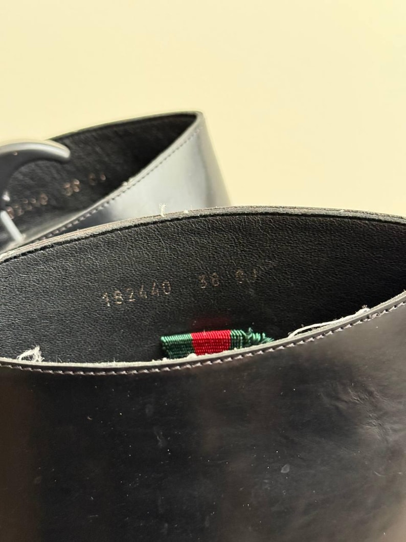 Op de afbeelding: Close-up van de binnenkant van een zwarte leren schoen. De schoen heeft een zwarte binnenzool met de nummers "182440 36" in het wit gedrukt. Een groen, rood en wit gestreept lint is zichtbaar.