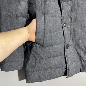 May include: A dark gray quilted jacket with a button closure. The jacket has a pocket on the left side.