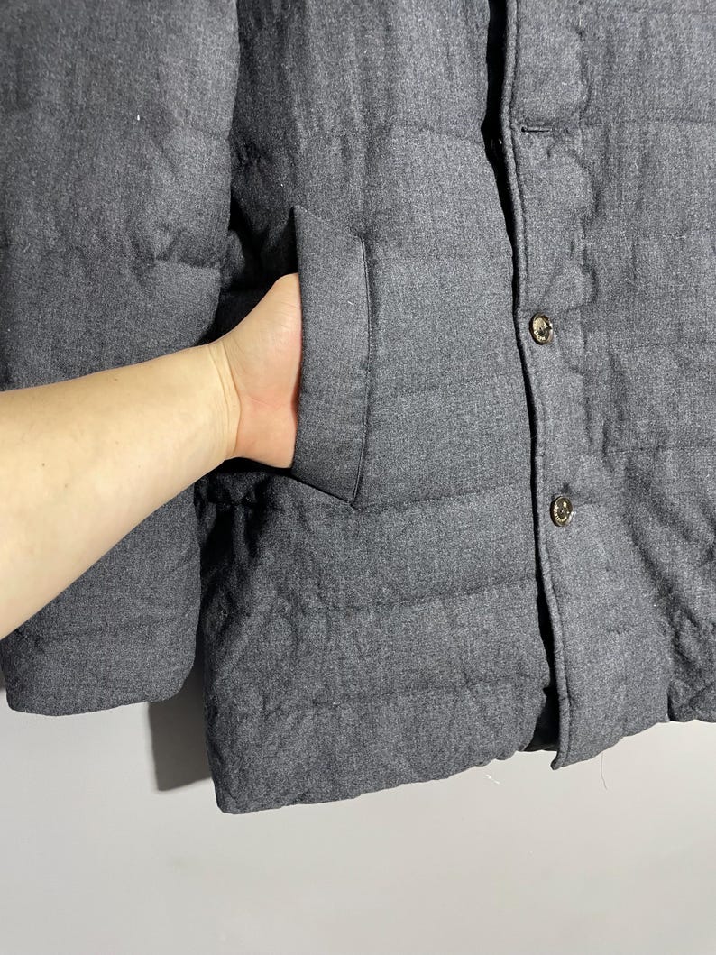 May include: A dark gray quilted jacket with a button closure. The jacket has a pocket on the left side.