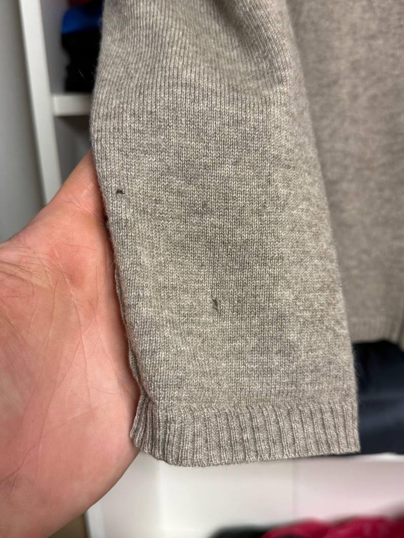 Pu&ograve; includere: Primo piano di una manica di maglione grigio chiaro. La manica &egrave; realizzata in tessuto a maglia con polsino a coste. Il maglione ha un design semplice e classico, adatto all'abbigliamento casual. Il tessuto appare morbido e confortevole.