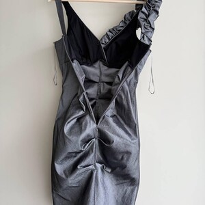 Puede incluir: Un vestido gris sin mangas con cuello en V y una sola correa. El vestido tiene un dise&ntilde;o fruncido en el corpi&ntilde;o y el hombro, y est&aacute; colgado de una percha de madera. El vestido est&aacute; hecho de una tela brillante.