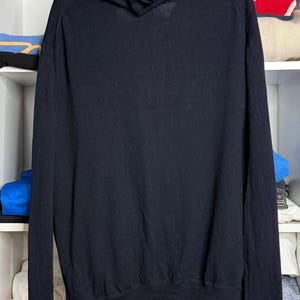 May include: Black hooded sweatshirt with a full-length zipper. The sweatshirt is made of a soft material and features a hood and long sleeves. The garment is displayed on a shelf with other clothing items.