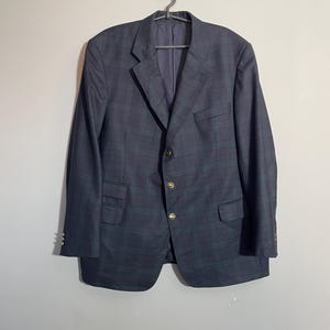 May include: A dark blue blazer with a plaid pattern and gold buttons. The blazer has a single-breasted closure and a notched lapel.