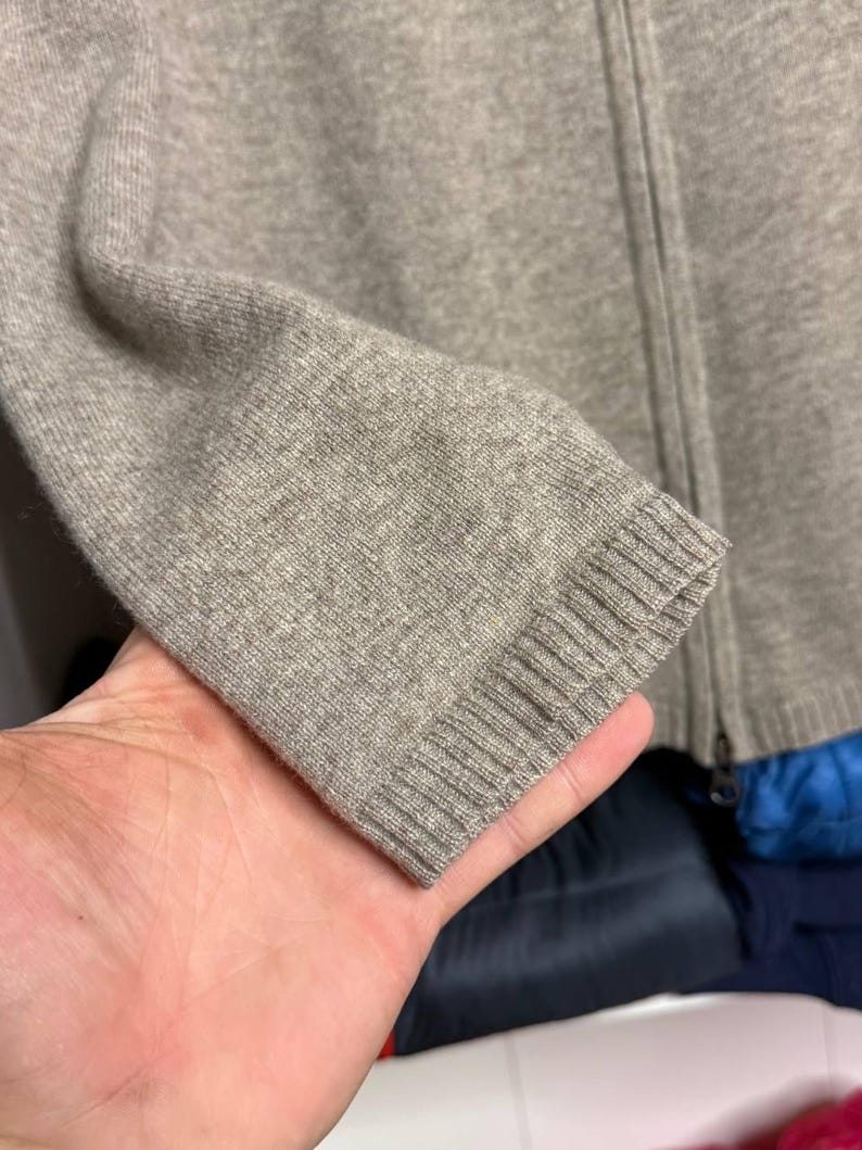 Pu&ograve; includere: Primo piano di un maglione con zip marrone chiaro. La manica &egrave; visibile, mostrando il polsino a coste e la trama del tessuto a maglia. Anche la cerniera &egrave; visibile.