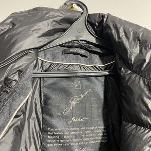 May include: A black jacket with a black label that reads "Mantecore Jacket". The label has gold text that says "The research, the cutting and the care of details, that feature our garments, totally reflect the tailoring tradition. The desire to create an exclusive garment, both for quality and peculiarity, guarantees a particular and a preciousness image. World".
