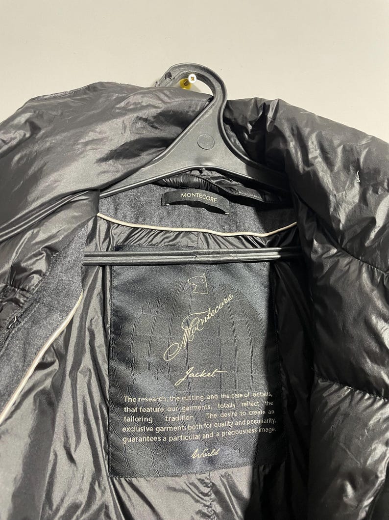 May include: A black jacket with a black label that reads "Mantecore Jacket". The label has gold text that says "The research, the cutting and the care of details, that feature our garments, totally reflect the tailoring tradition. The desire to create an exclusive garment, both for quality and peculiarity, guarantees a particular and a preciousness image. World".