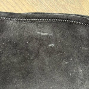 May include: Close-up of a section of black fabric with a visible seam at the top. The fabric has a slightly textured appearance with some light-colored marks and small fibers scattered across its surface.
