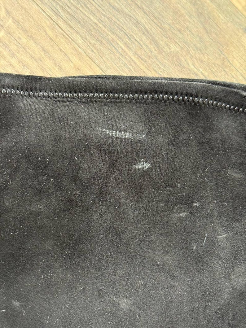 May include: Close-up of a section of black fabric with a visible seam at the top. The fabric has a slightly textured appearance with some light-colored marks and small fibers scattered across its surface.