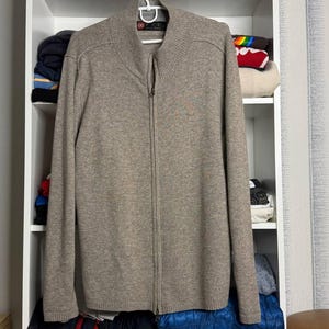Pu&ograve; includere: Un maglione con zip marrone chiaro con collo alto, appeso a una gruccia bianca. Il maglione &egrave; realizzato in un materiale morbido e ha una cerniera a tutta lunghezza. Il maglione &egrave; esposto in una scaffalatura bianca.