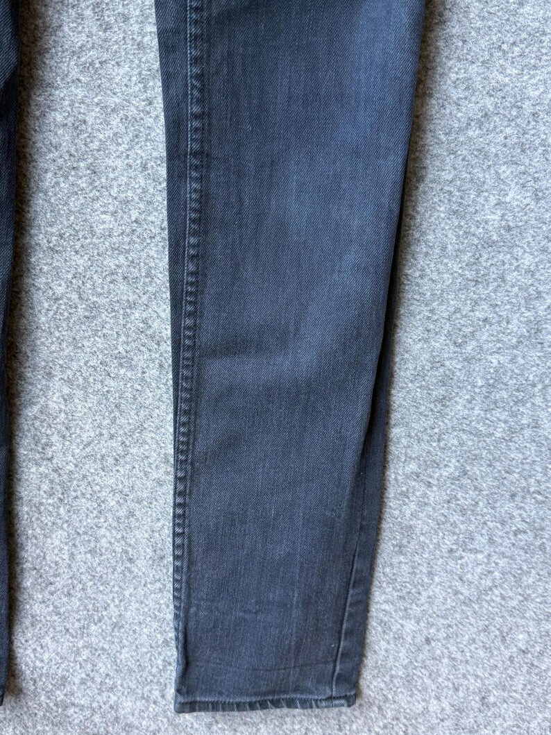 Op de afbeelding: Een donkergrijze spijkerbroek van denim met een klassieke vijf-pocket constructie en zichtbare verticale stiksels langs de buitenste broekspijpen. De stof heeft een subtiele, uniforme textuur die kenmerkend is voor katoenen denim met een vervaagde antracietkleurige afwerking.